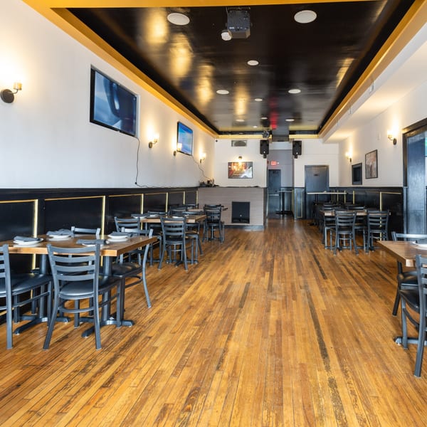 Empty restaurant dining room with wooden floors, black tables, chairs, and a black and gold ceiling.