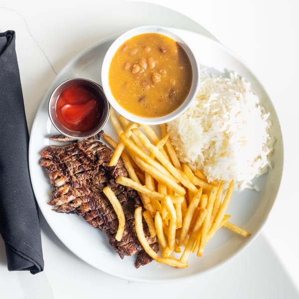 Grilled steak, french fries, white rice, and a bowl of beans with a side of ketchup.