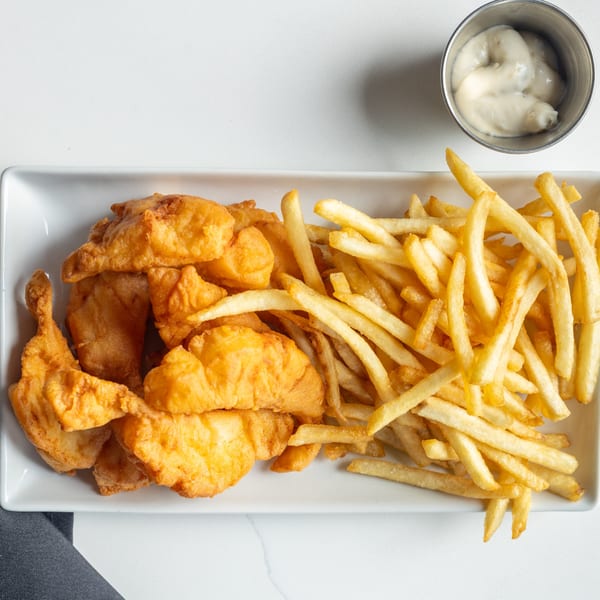 Crispy golden fish and chips with a side of tartar sauce on a white rectangular plate.