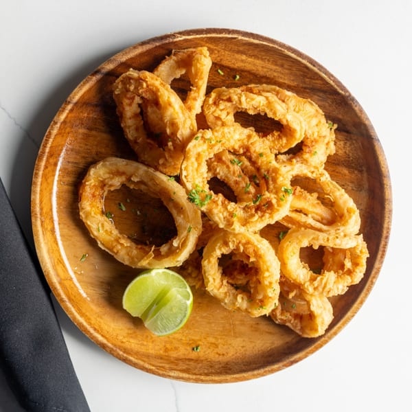 Crispy golden fried calamari rings with parsley and a lime wedge on a wooden plate.