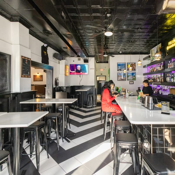 A vibrant bar interior with a black and white chevron floor, a woman at the bar, and a bartender.